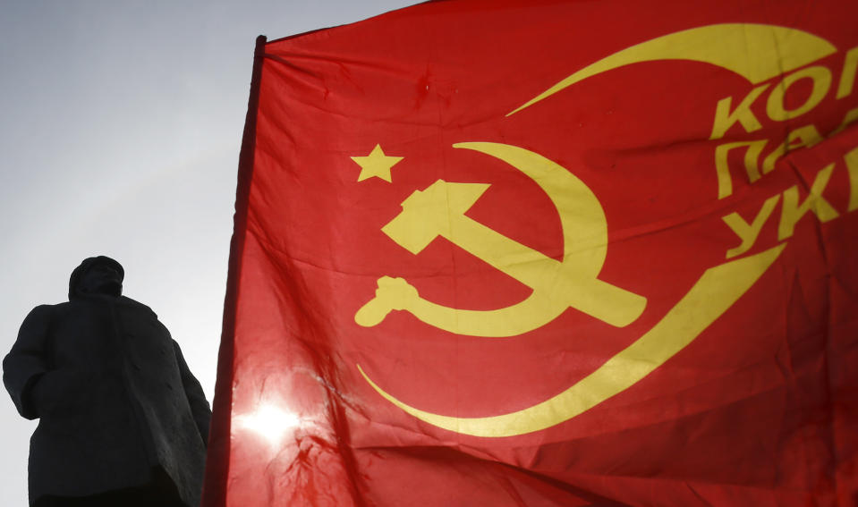 A man waves a communists flag in front of the monument of Soviet Union founder Vladimir Lenin, during a Victory Day celebration, which commemorates the 1945 defeat of Nazi Germany, in the center of Slovyansk, eastern Ukraine, Friday, May 9, 2014. Putin's surprise call on Wednesday for delaying the referendum in eastern Ukraine appeared to reflect Russia's desire to distance itself from the separatists as it bargains with the West over a settlement to the Ukrainian crisis. But insurgents in the Russian-speaking east defied Putin's call and said they would go ahead with the referendum. (AP Photo/Darko Vojinovic)