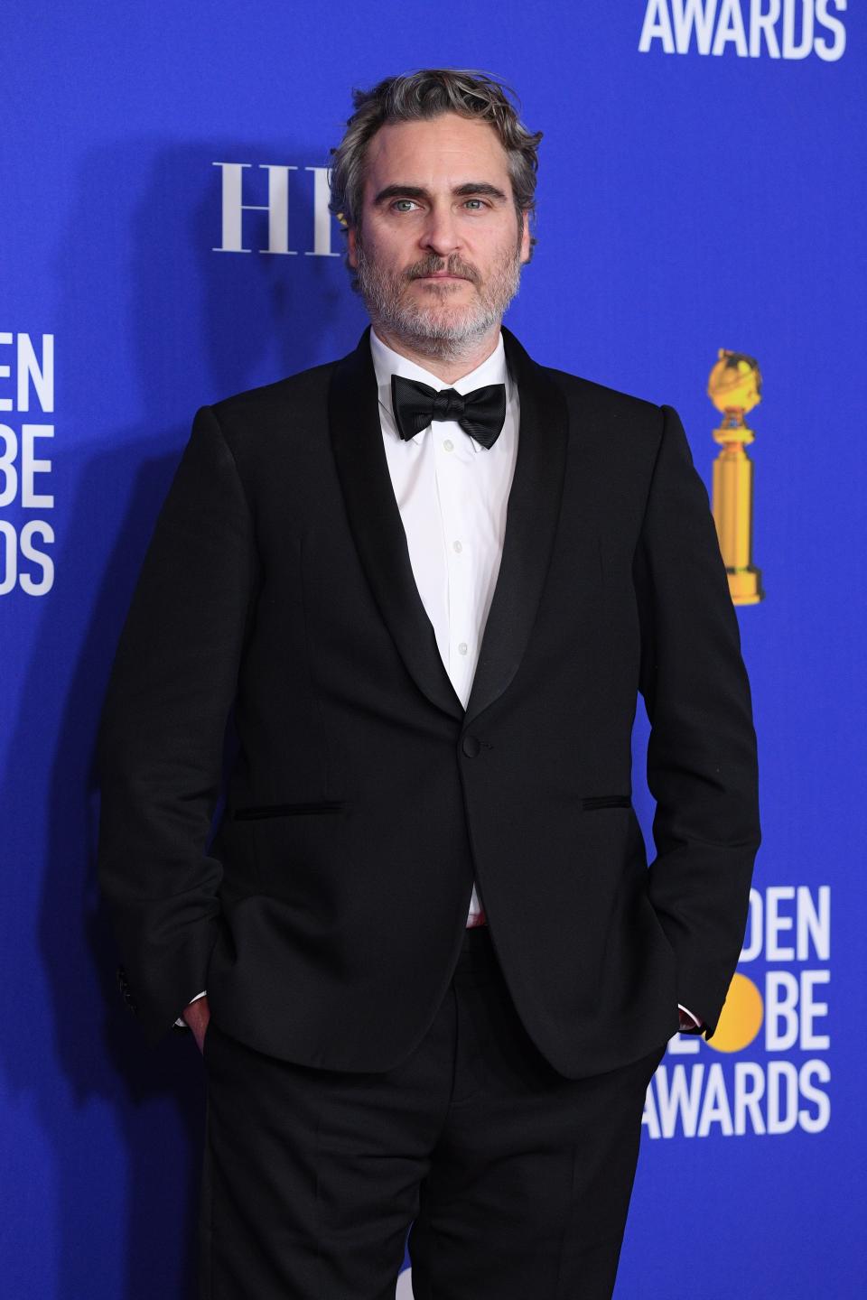 Joaquin Phoenix posing in a classic black suit and bow tie at the Golden Globe Awards