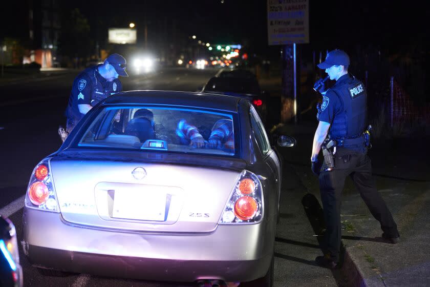 Gresham Police Sgt. Travis Garrison, left, and Officer Ryan Gomez look inside a vehicle during a traffic stop in Gresham, Ore., Thursday, July 21, 2022. Gresham, a Portland suburb, has seen an increase in fatal shootings and gun violence at the same time as it has a shortage of officers. To address the situation, the department has shut down all of its specialized units except for its mental health unit and shifted all of its detectives to work homicides. (AP Photo/Craig Mitchelldyer)