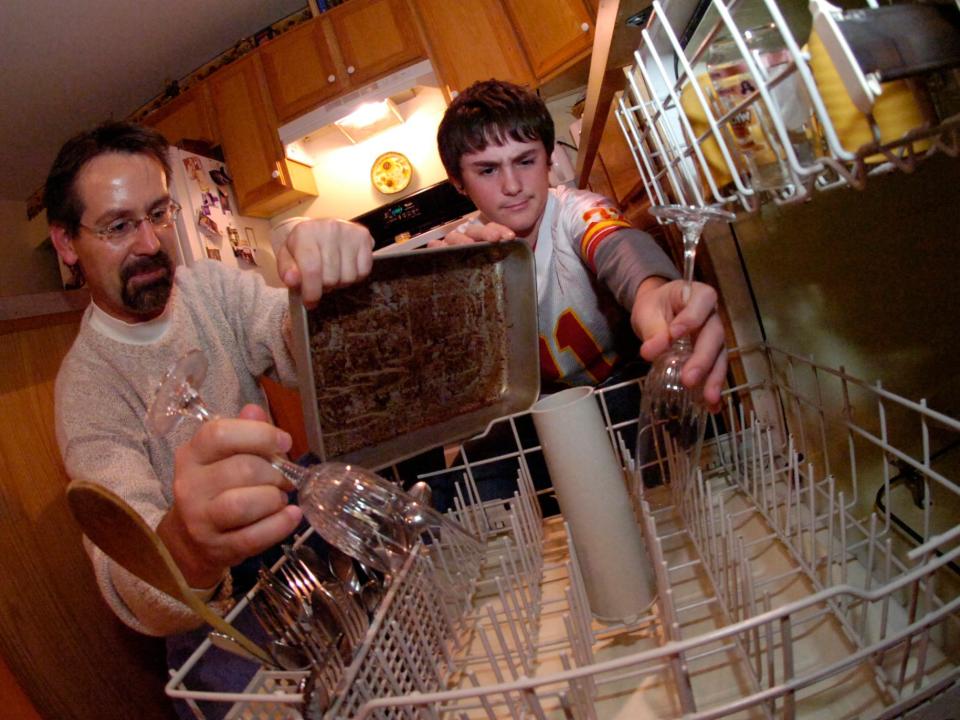 Father and son put items in dishwasher.