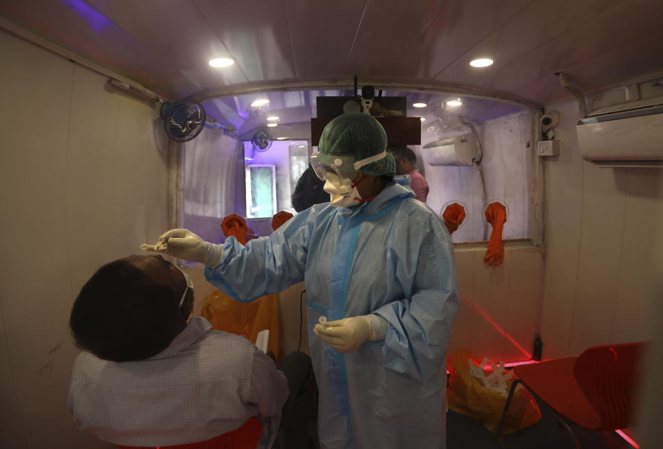 A health worker inside a mobile lab takes nasal swab sample for COVID- 19 testing through rapid antigen methodology in New Delhi, India, Monday, Aug. 10, 2020. India is the third hardest-hit country by the pandemic in the world after the United States and Brazil. (AP Photo/Manish Swarup)