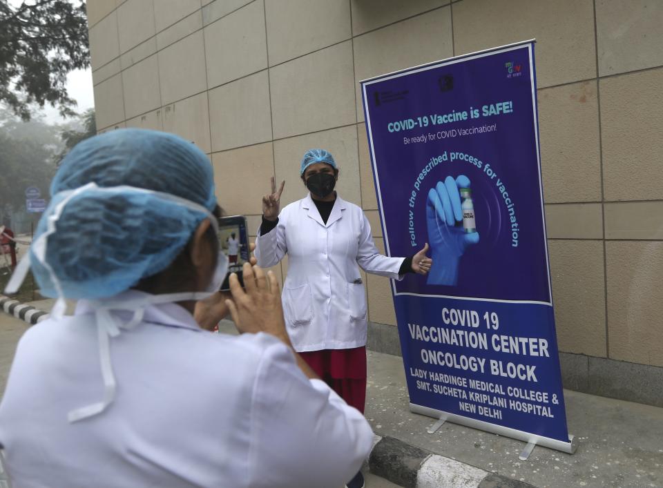 A health worker gestures as she gets her photograph taken next to a COVID-19 vaccination banner at a hospital in New Delhi, India, Saturday, Jan. 16, 2021. India started inoculating health workers Saturday in what is likely the world's largest COVID-19 vaccination campaign, joining the ranks of wealthier nations where the effort is already well underway. (AP Photo/Manish Swarup)