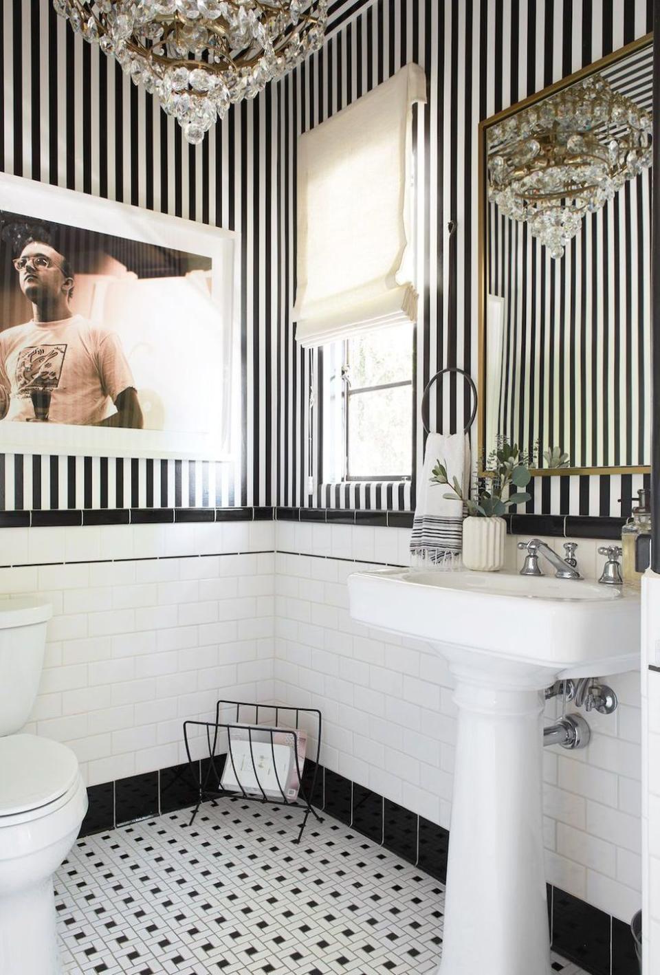 <p>This sweet bathroom designed by Leanne Ford is a lesson in small upgrades that can make an outdated space feel brand new. The contrast between the hyper-realist, gritty photograph against the classic black and white striped wallpaper and glitzy chandelier create a nice juxtaposition. She added an accent magazine rack, custom linen curtains, a hand towel ring, and a case to polish things off without having to replace the existing sink and toilet. </p>