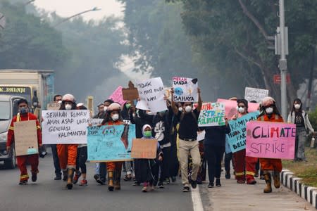 Youths walk with signs through the main road during a Global Climate Strike rally as smog covers the city due to the forest fires in Palangka Raya