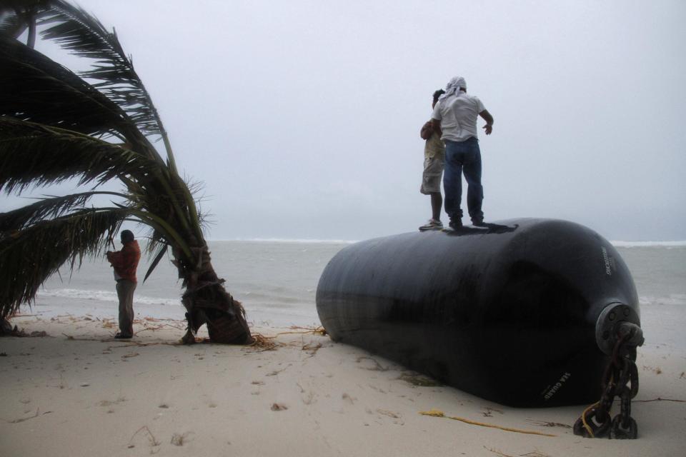 Men stand on top of a marine fender that was ripped from a dock after Hurricane Ernesto made landfall overnight in Mahahual, near Chetumal, Mexico, Wednesday, Aug. 8, 2012. (AP Photo/Israel Leal)