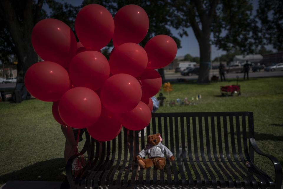 A teddy bear sits alone on a park bench under a bouquet of red balloons at the memorial site for victims of the mass shooting at Robb Elementary School in the town square of Uvalde, Texas on Saturday, May 28, 2022. In a town as small as Uvalde, even those who didn't lose their own child lost someone. Some say now that closeness is both their blessing and their curse: they can lean on each other to grieve. But every single one of them is grieving. (AP Photo/Wong Maye-E)