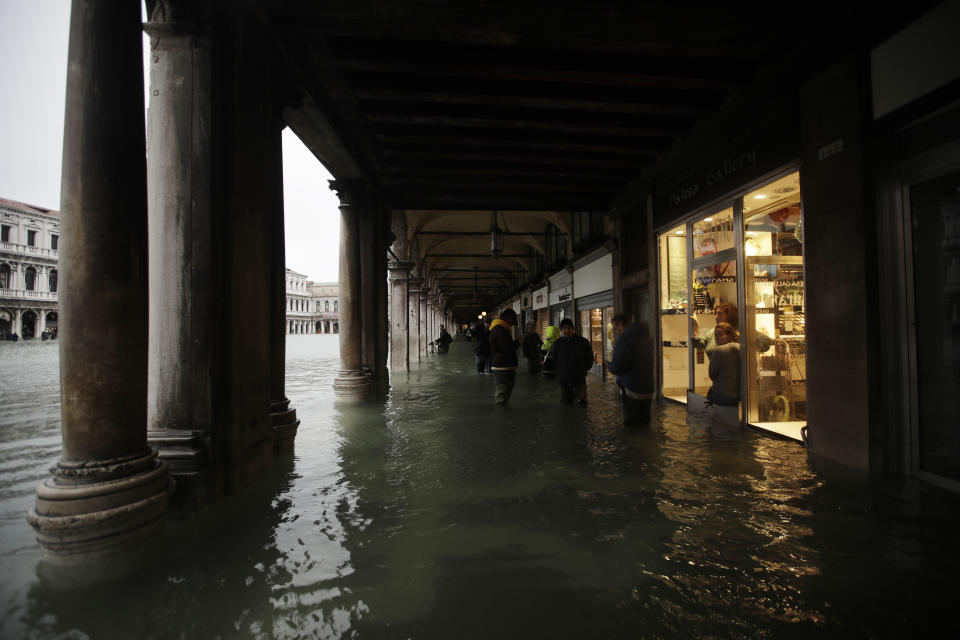 People stand near shops in a flooded St. Mark's Square in Venice, Italy, Friday, Nov. 15, 2019. The high-water mark hit 187 centimeters (74 inches) late Tuesday, Nov. 12, 2019, meaning more than 85% of the city was flooded. The highest level ever recorded was 194 centimeters (76 inches) during infamous flooding in 1966. (AP Photo/Luca Bruno)