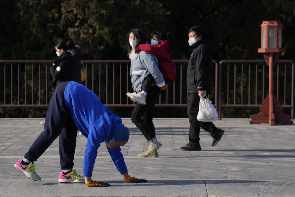 Visitors wearing masks watch as a resident walks on all four limbs as a form of exercise in the Temple of Heaven park in Beijing, Thursday, Dec. 8, 2022. In a move that caught many by surprise, China announced a potentially major easing of its rigid "zero-COVID" restrictions, without formally abandoning the policy altogether. (AP Photo/Ng Han Guan)