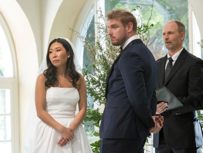 A woman in a strapless wedding dress with long, curled hair and a taller man wearing a navy blue tuxedo.