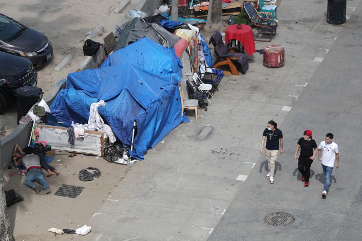 People walk past homeless encampments on the Venice Beach boardwalk in Los Angeles.