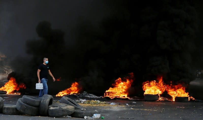 A demonstrator wears a face mask as he walks near burning tires during a protest over deteriorating economic situation in Jdeideh