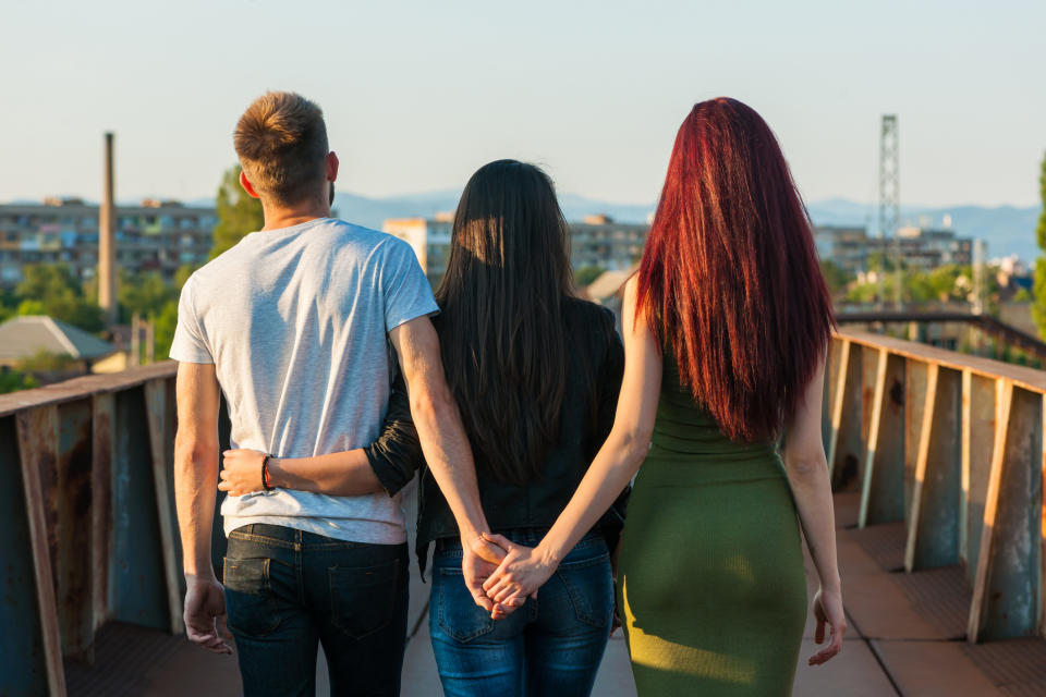 Three people are walking on a bridge, holding each other around the waist, facing away. They appear to be family or close friends