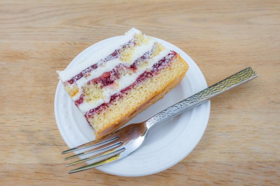 A slice of cake with white cake, cream, and strawberry jam layers on a plate next to a metal fork 