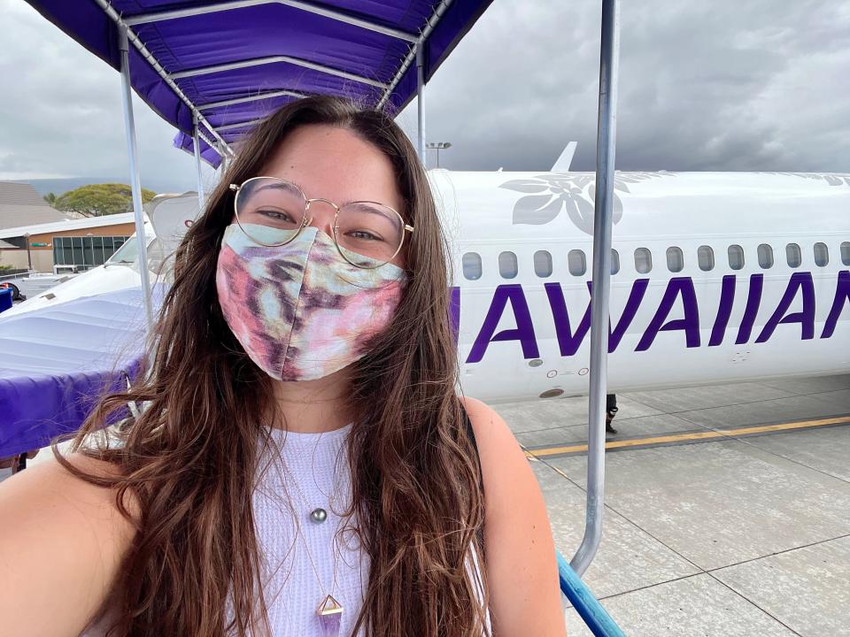 the writer with a mask on posing in front of hawaiian airlines plane