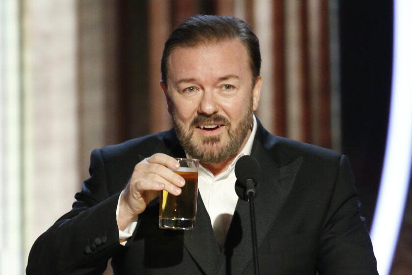 Ricky Gervais, in a black suit, holds a glass in the air while hosting the 77th Annual Golden Globe Awards