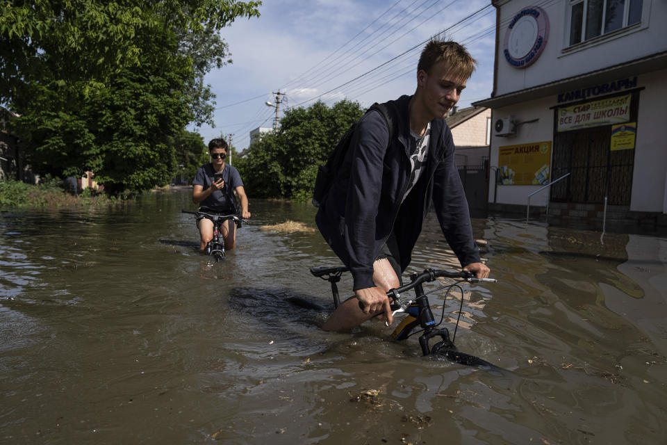 災區民眾騎著自行車通過淹水街道。(畫面來源：AP)