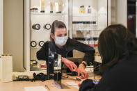 A retail worker wearing a face mask serves a customer behind a shield as she processes a sale at a large retail department store in Melbourne, Australia, Wednesday, Oct. 28, 2020. Australia’s second largest city of Melbourne which was a coronavirus hotspot emerges from a nearly four-months lockdown, with restaurants, cafes and bars opening and outdoor contact sports resuming on Wednesday. (AP Photo/Asanka Brendon Ratnayake)