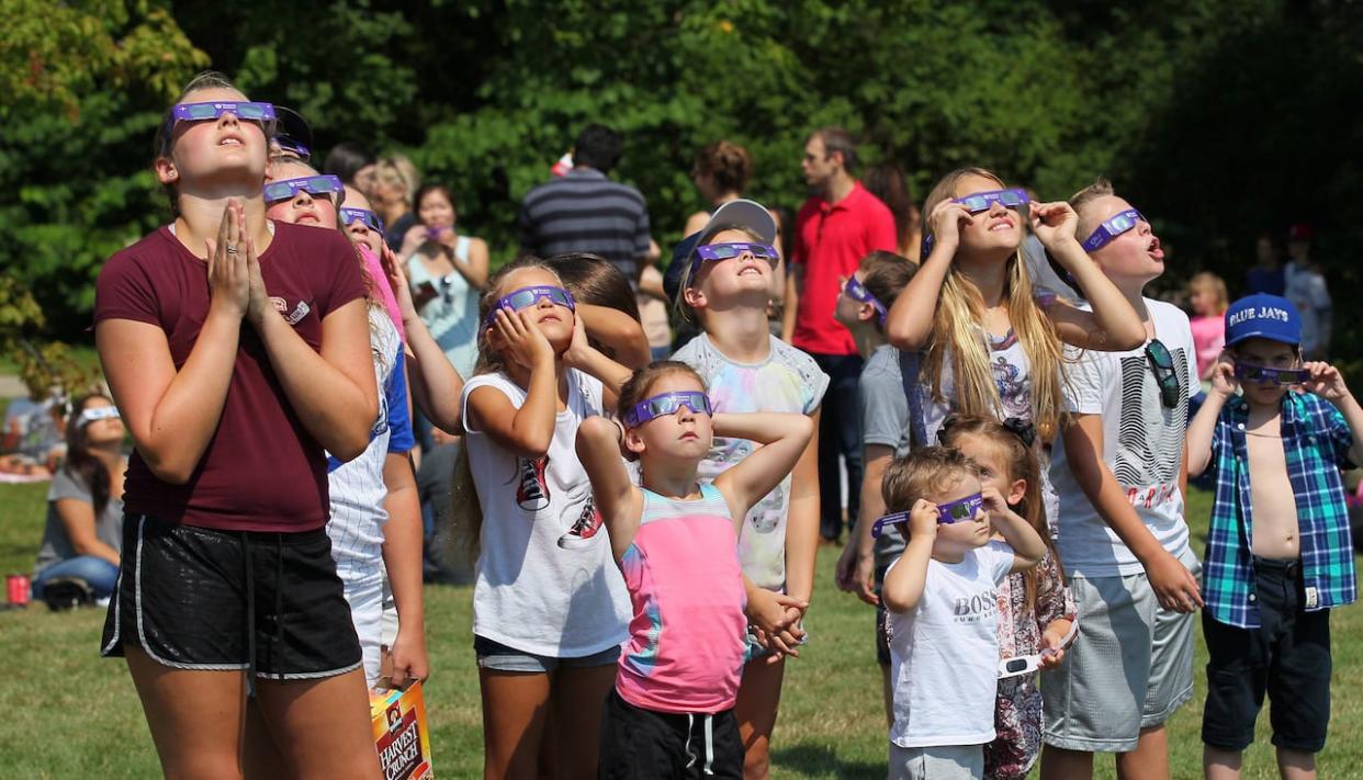 A group of children join hundreds of people gathered at Western University to view the partial solar eclipse, in London, Ont., in 2017. Much of Quebec is expected to have good weather for the eclipse on April 8, prompting some to change their travel plans to stay in the province.  (Dave Chidley/The Canadian Press - image credit)