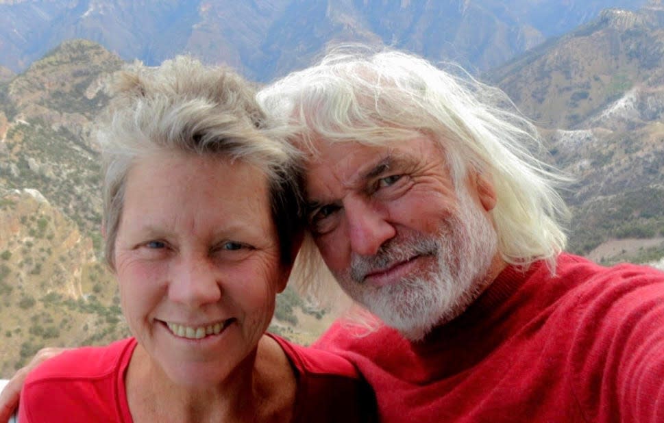 An older woman and man wearing red shirts and posing for a photo with mountains behind them.