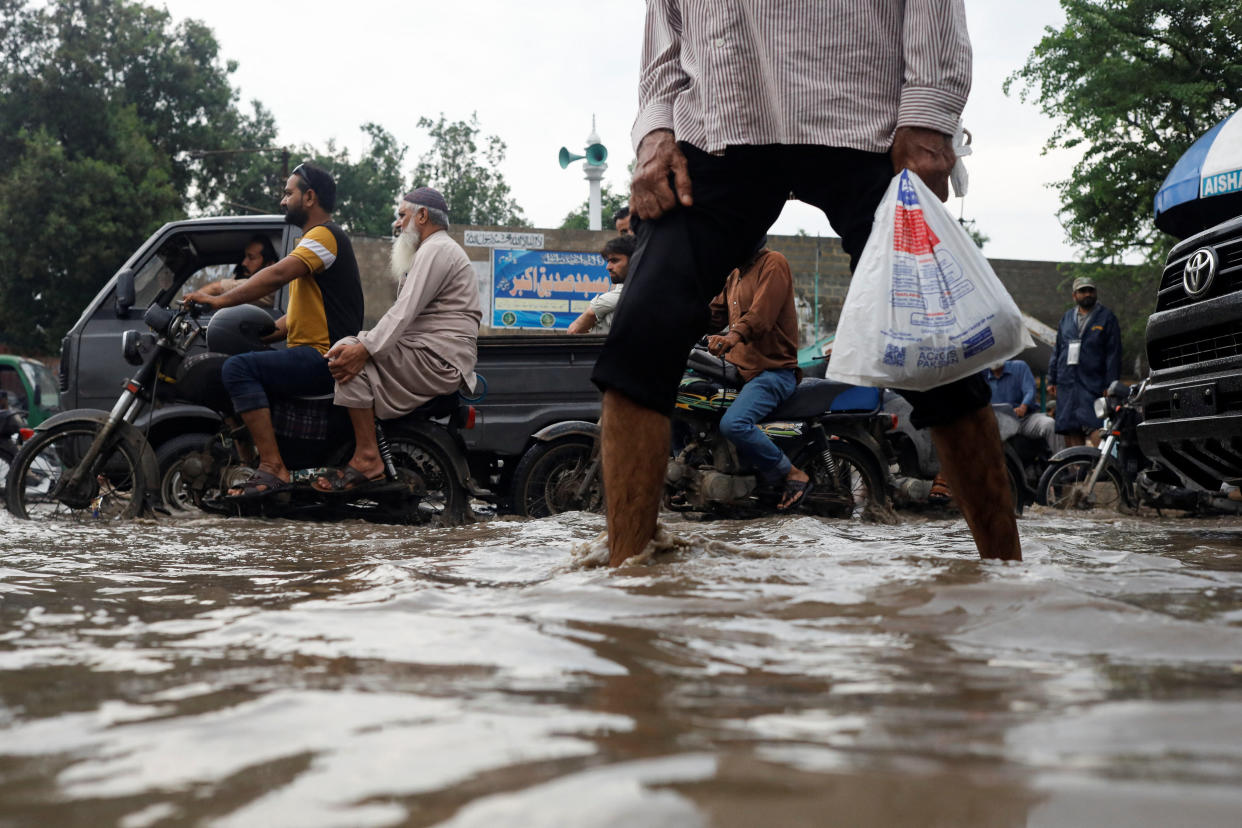 People make their way on a flooded road in Karachi on foot, on motorbikes and in cars.