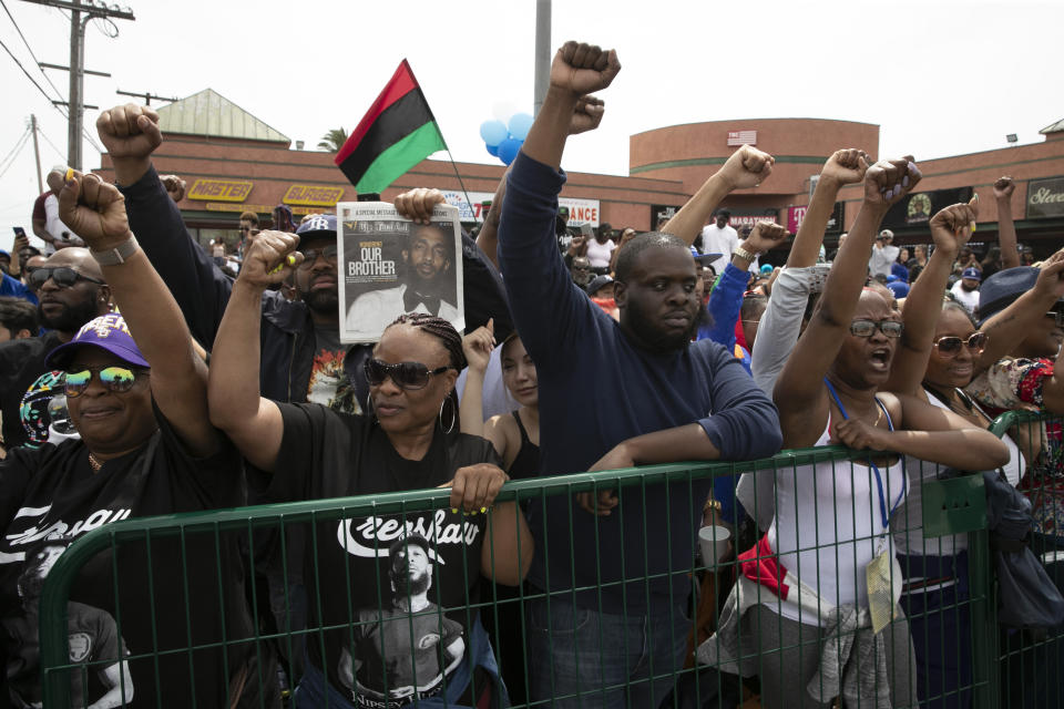 People hold up their fists while waiting for a hearse carrying the casket of slain rapper Nipsey Hussle to pass by in front of Hussle's clothing store The Marathon Thursday, April 11, 2019, in Los Angeles. The 25-mile procession traveled through the streets of South Los Angeles after his memorial service, including a trip past Hussle's clothing store, The Marathon, where he was gunned down March 31. (AP Photo/Jae C. Hong)