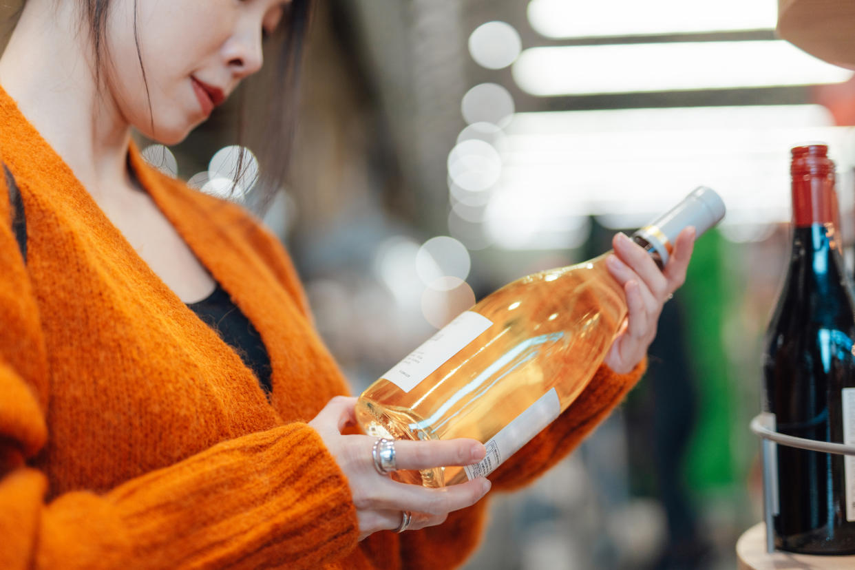 A woman examines a wine bottle in a store.