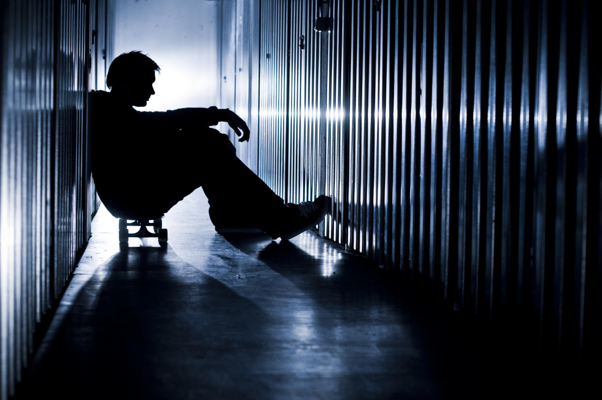The silhouette of a young person sitting on a skateboard in a dark hallway.