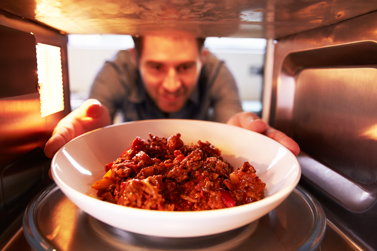 man putting leftover chili into microwave oven to cook