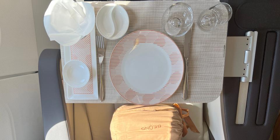 A top-down shot of the dinner service onboard Beond A319, with white crockery with orange accents, two glasses, and a couple pots