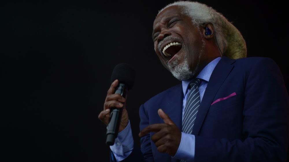 Billy Ocean with long white hair holding a microphone and laughing