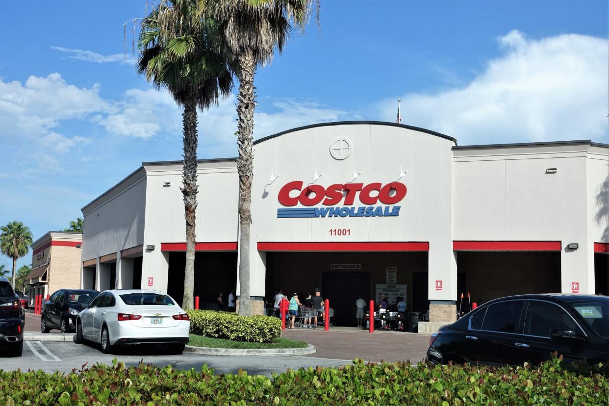 A Costco Wholesale store in West Palm Beach, Florida, USA. Costco is a combined department store and supermarket that sells in bulk and requires a club membership to shop. Customers are visible at the store entrance and cars are in the parking lot.
