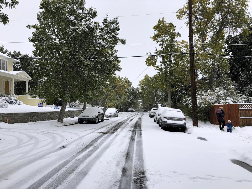 Pedestrians make their way along a snow covered street lined with trees that still have their leaves during a fall snowstorm in Helena, Mont., on Sunday, Sept. 29, 2019. Strong winds and heavy snow caused power outages and temporary road closures in northwestern Montana as a wintry storm threatened to drop several feet of snow in some areas of the northern Rocky Mountains. (AP Photo/Matt Volz)