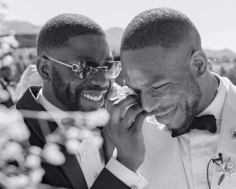 A man wipes a tear from a groom's face on his wedding day.