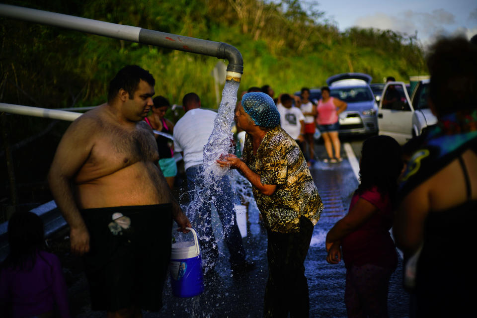 Residentes de Utuado, Puerto Rico, se aglomeran frente a tuberías que traían agua de un riachuelo el 14 de octubre del 2017, tras el paso del huracán María que causó devastación en la isla. (AP Photo/Ramón Espinosa, File)