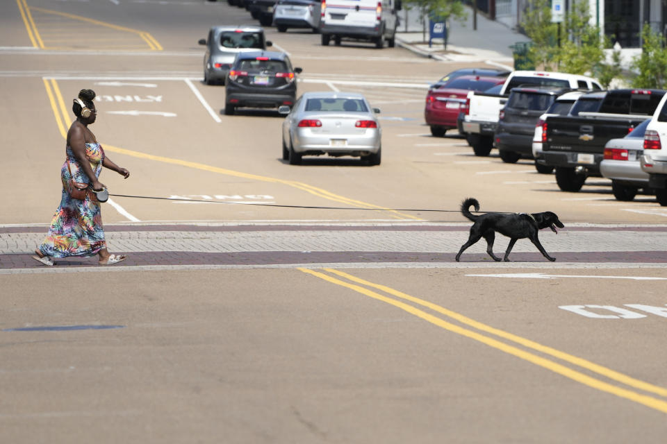 Una mujer pasea a su perro poco después del mediodía el jueves 29 de junio de 2023, por el centro de Jackson, Mississippi. (AP Foto/Rogelio V. Solis)