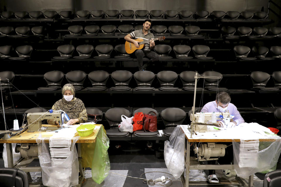 Volunteers wearing face masks to curb the spread of the new coronavirus sew new masks as a man plays guitar for them at the Hafez theater hall in downtown Tehran, Iran, Wednesday, April 15, 2020. (AP Photo/Ebrahim Noroozi)