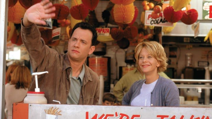 Tom Hanks puts his hand up while standing next to Meg Ryan.