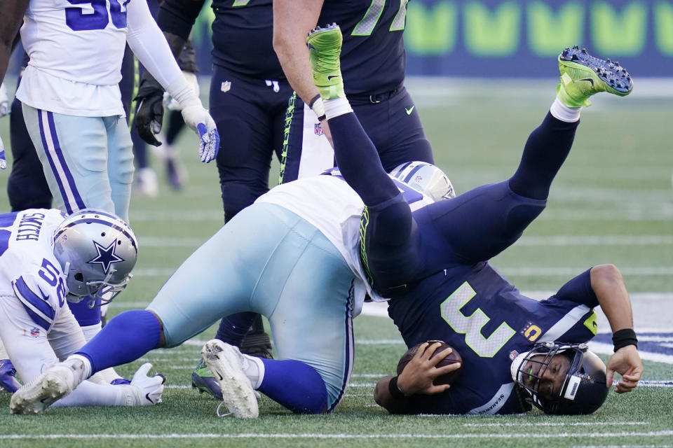 Seattle Seahawks quarterback Russell Wilson is upended after he was sacked by Dallas Cowboys defensive tackle Antwaun Woods, center, during the second half of an NFL football game, Sunday, Sept. 27, 2020, in Seattle. (AP Photo/Elaine Thompson)