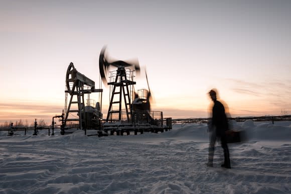 Pump jack and engineer on a winter sunset sky background.