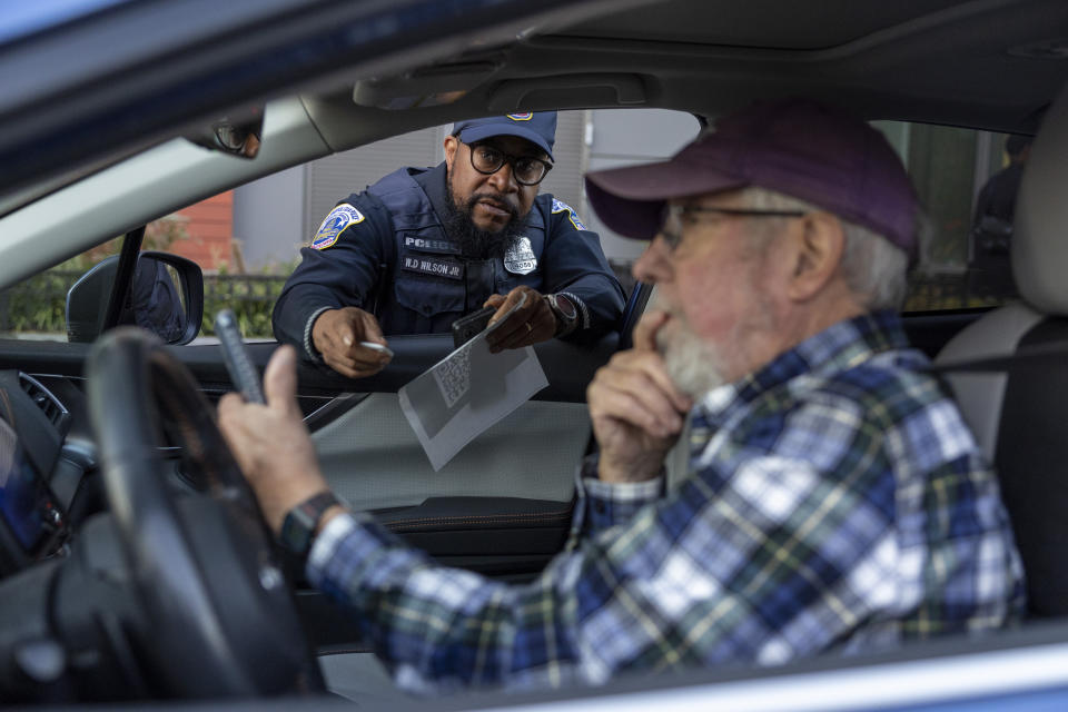 Metropolitan Police Department officer Muhammad Lewis explains to Nils Bruzelius how to use a Tile tracker during an event where police officers distributed mobile tracking devices for cars to drivers in an attempt to curb a rise in crime in Washington on Tuesday, Nov. 7, 2023. (AP Photo/Amanda Andrade-Rhoades)