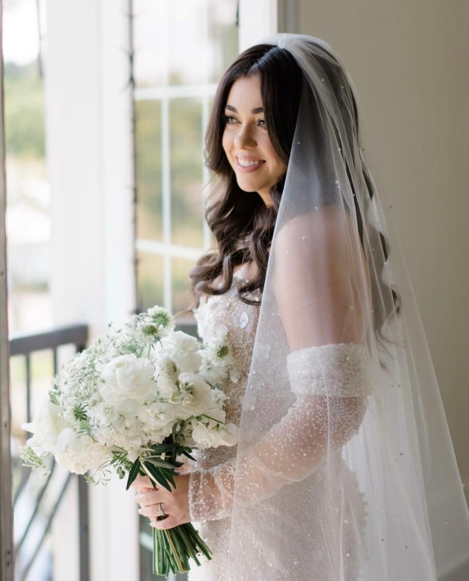 A bride poses in her wedding dress and veil holding a veil.