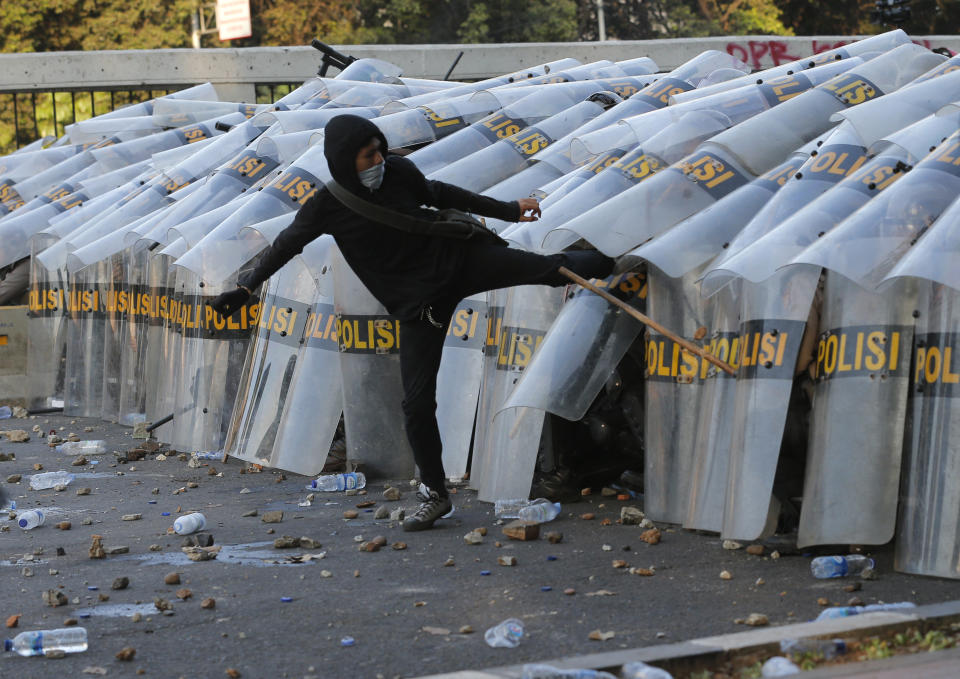 A student protester kicks the shield of riot police officers during a clash in Jakarta, Indonesia, Monday, Sept. 30, 2019. Thousands of Indonesian students resumed protests on Monday against a new law they say has crippled the country's anti-corruption agency, with some clashing with police. (AP Photo/Tatan Syuflana)