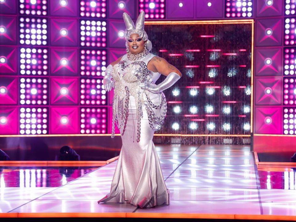 Malaysia Babydoll Foxx walks the runway in episode 3 in a silver gown with silvery hair and gloves.