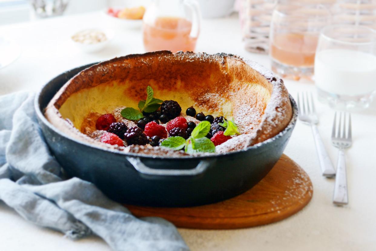 Fresh homemade dutch baby pancake with powdered sugar, fresh berries and mint for breakfast with a glass of milk and apple juice on a light background. Delicious  breakfast in a sunny interior.