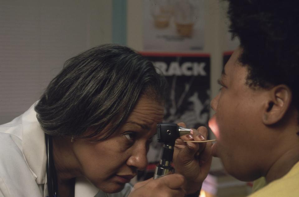 A Black female doctor peers into the mouth of a patient.