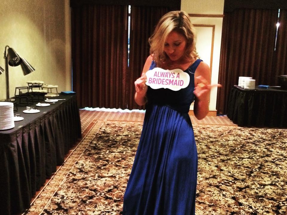 jen glantz holding an always a bridesmaid sign at a wedding reception