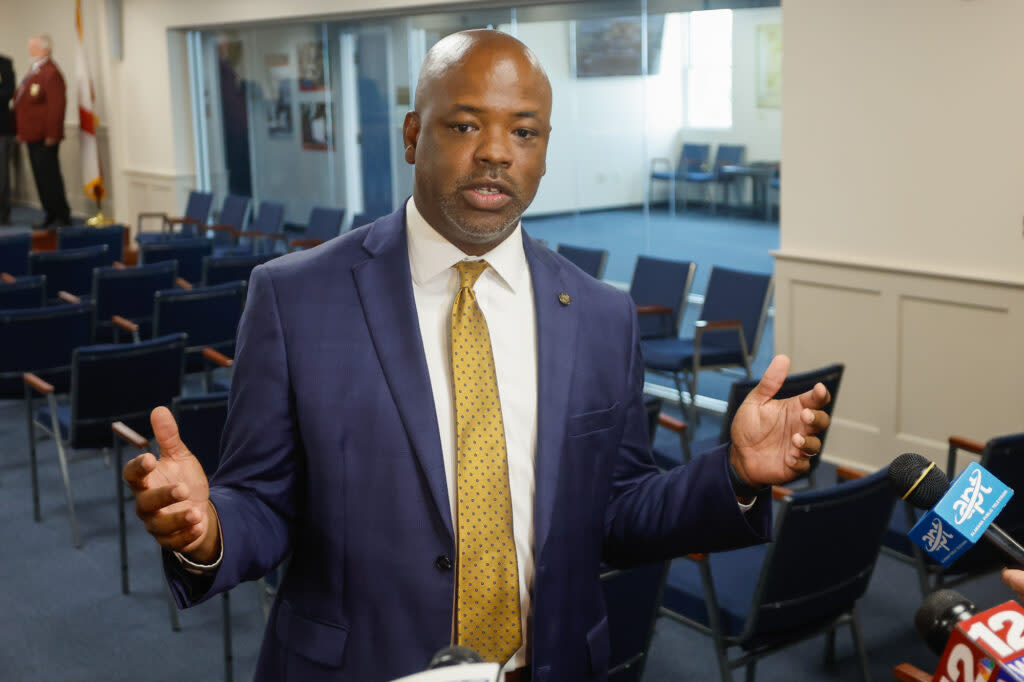 A man in a blue suit and yellow tie gestures.