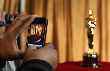 A man photographs an Oscar statuette using his phone at the "Meet the Oscars" exhibit at Grand Central Station in New York February 23, 2011. REUTERS/Brendan McDermid/Files