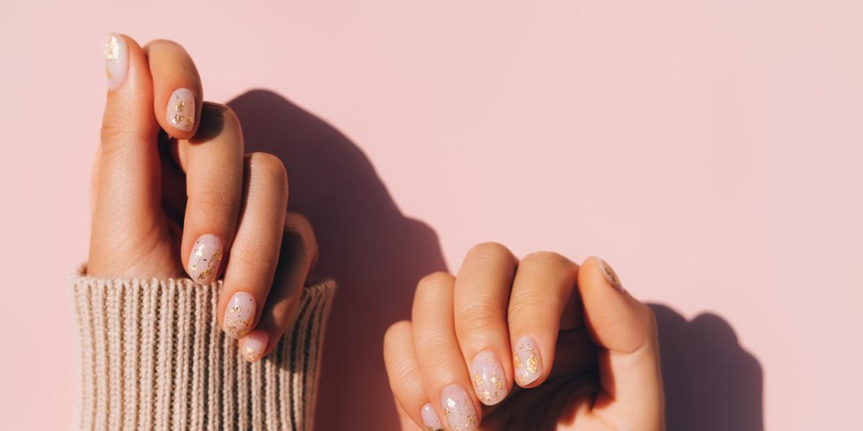 glowing hands in sweater with knitted sleeves and with nude color manicure with gold particles on pink table trendy colors of the year