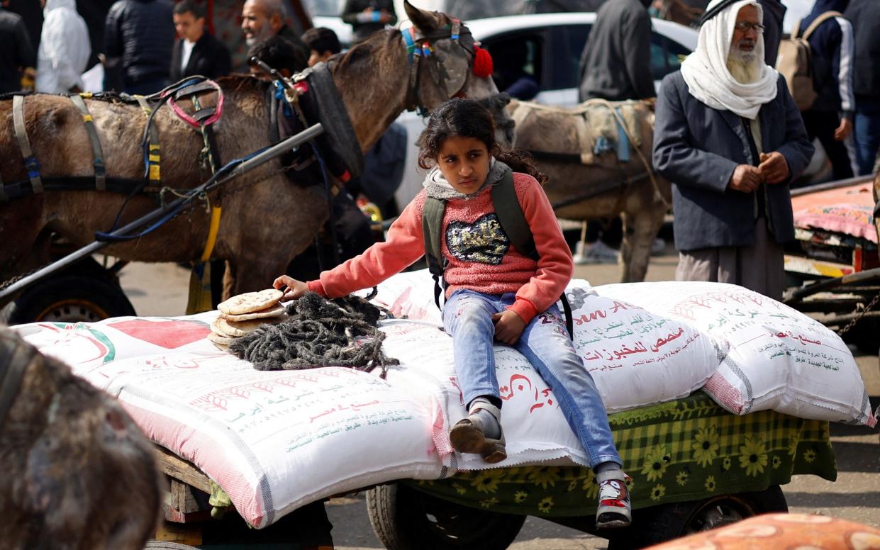 A Palestinian girl sits on bags of flour distributed by the United Nations Relief and Works Agency